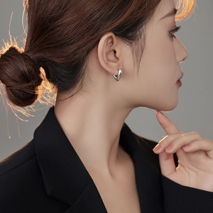 Close-up of heart shaped silver hoop earrings with polished metal texture on model