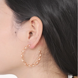 Close-up of a gold twisted wave hoop earring worn by a model in a minimalist style