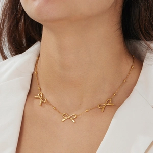 Detail of gold bow pendants and bead chain on a minimalist stainless steel necklace
