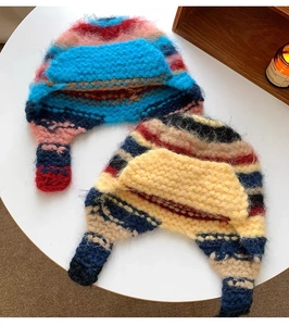 Flat lay of colorful thick knit beanies with ear flaps on a white round table