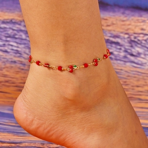 Close-up of a gold cherry anklet with red beads and green leaf charms on an ankle