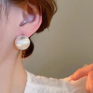 Close-up of elegant oversized pearlescent floral stud earrings worn on earlobe