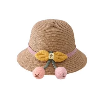 Kids straw sun hat with pink ribbon, yellow bow and cherry pom-poms on white background