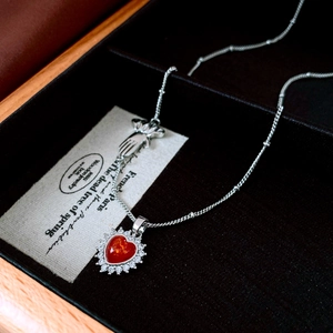 Macro detail of red heart pendant with zircon halo and hand charm on silver chain