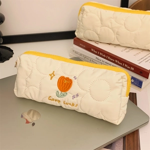 Detail of quilted beige tulip embroidery pouch and zipper stationery storage on a desk