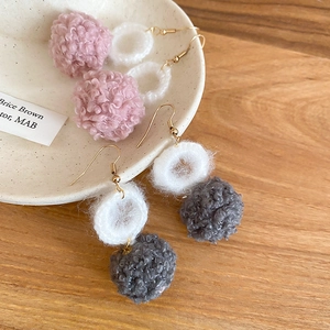 Dettaglio di orecchini invernali con pompon di peluche rosa e grigi e ganci dorati