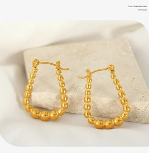 Macro shot of gold beaded U-shaped earrings on stone surface with white silk accent