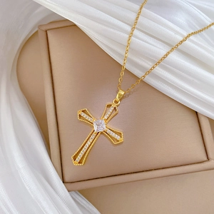 Close-up of gold cross necklace featuring a square white gemstone and crystal inlay
