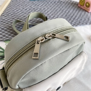 Détail des doubles fermetures éclair argentées et de la texture en toile du petit sac vert clair