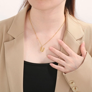Close-up of a gold letter U pendant with rhinestones on a delicate bead chain necklace