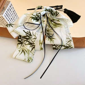 Detailed shot of white bow hair clip with green bamboo patterns and long black ribbons