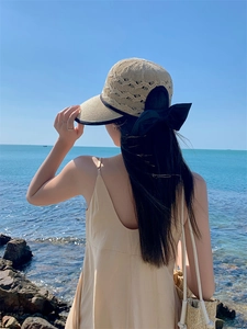 Detail of summer straw hat with black bow decoration against a blue ocean backdrop