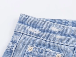 Détail de jean en denim bleu clair avec rivets métalliques et taille à effet usé