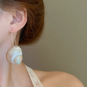 Close-up of model wearing unique shell-shaped hoop earrings with iridescent white luster
