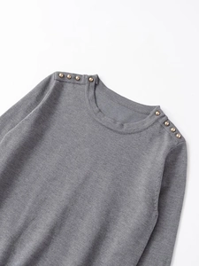 Detail of grey knit sweater showing golden decorative buttons on shoulder and ribbed collar