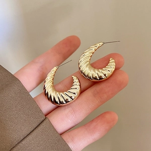Close-up of golden croissant-style earrings showing spiral texture and metallic finish