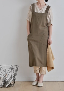 Olive green linen apron with H-back straps and two front pockets in minimalist home setting