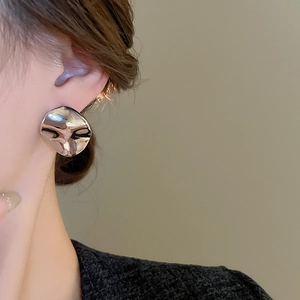 Detailed close-up of a silver irregular round metal stud earring on a female model