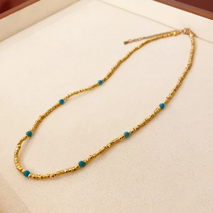 Détail du collier perlé doré avec accents turquoise et chaîne d'extension en métal réglable