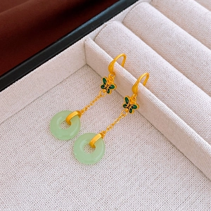 Détail des boucles d'oreilles papillon dorées avec pendentif jade sur présentoir blanc