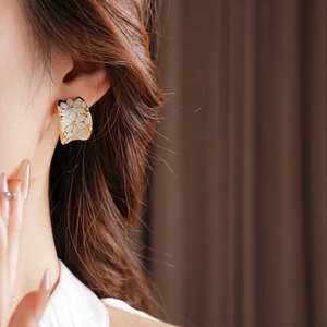 Gros plan de boucles d'oreilles dorées en C avec fleurs blanches aspect nacre