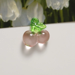 Macro shot of a translucent pink cherry acrylic pendant with green leaves for DIY jewelry