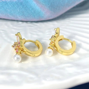 Gros plan détaillé de boucles d'oreilles papillon dorées avec zircons roses et perle blanche