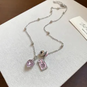 Silver beaded necklace with pink heart gem and winged enamel pendant on beige background