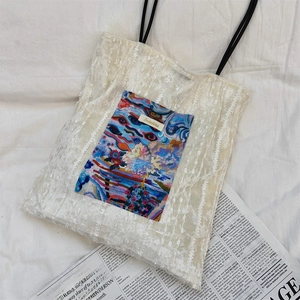 Detailed close-up of white lace tote bag with colorful artistic pocket on fabric background