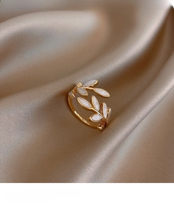 Detail of elegant gold leaf ring with white shell inlay on champagne silk background