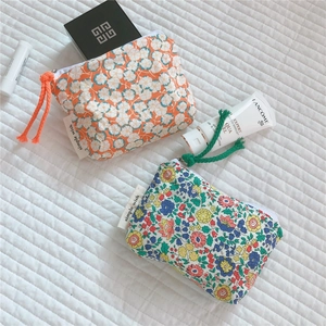 Close-up of floral cotton coin pouches with zippers and branded labels on white fabric