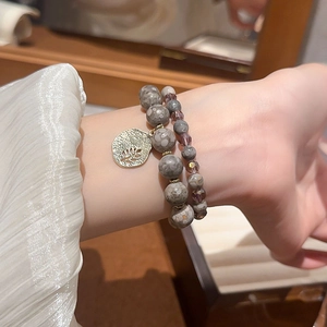 Close-up of double-layer beaded bracelet with natural grey stones and gold leaf pendant