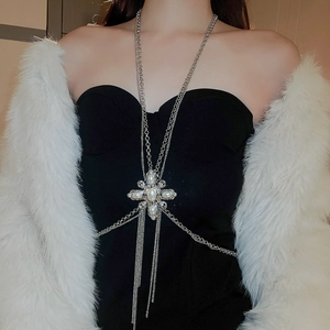 Macro detail of silver body chain featuring a pearl cross pendant and tassel fringes