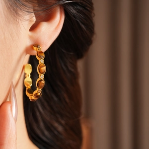 Dettaglio dell'orecchino a cerchio vintage in oro con occhio di tigre e cristalli su modella