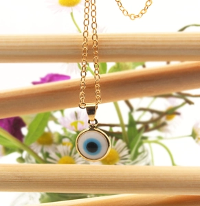 Detail shot of golden evil eye pendant necklace on a wooden stand with floral background