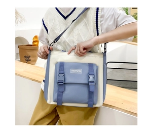 Detail view of blue and cream canvas crossbody bag with buckle front pocket on a model