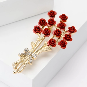 Elegant gold metal brooch with red rose bouquet and rhinestone bow on a white stand