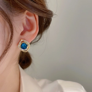 Close-up of elegant square blue zircon earrings with gold plating on female ear