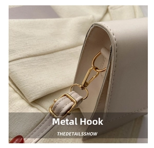 Detail of light gold hardware hook and adjustable leather strap on a beige crossbody bag