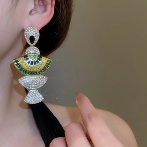 Detail of gold fan-shaped earring with green and yellow gems on female model