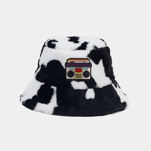 Detail of plush cow print bucket hat with retro cassette patch on a gray background