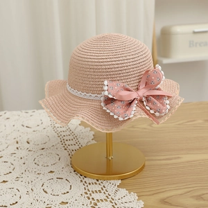 Détail du chapeau de paille rose avec dentelle et nœud floral sur support doré