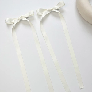 Detailed view of a pair of white satin bow hair clips with long ribbons in ballet style
