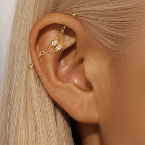 Close-up of golden industrial barbell earring with chain and clear zircon pendants