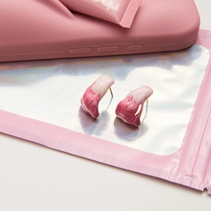 Detail of pink marble resin stud earrings on a holographic bag and phone case backdrop