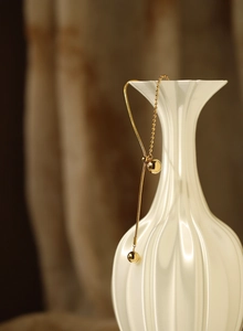 Detailed close-up of golden sphere pendants on snake chain necklace draped on ceramic vase