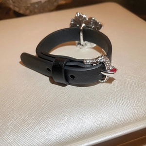 Detailansicht eines schwarzen Lederarmbands mit silberner Blume und rotem Edelsteinbesatz