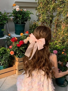 Detail of a large peach pink mesh bow hair clip with long ribbons on a model in a garden