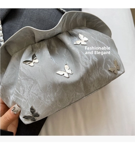 Detailed macro of silver pleated cloud bag featuring 3D metal butterfly ornaments