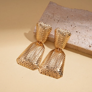 Macro detail of gold-finish geometric layered earrings with intricate woven texture